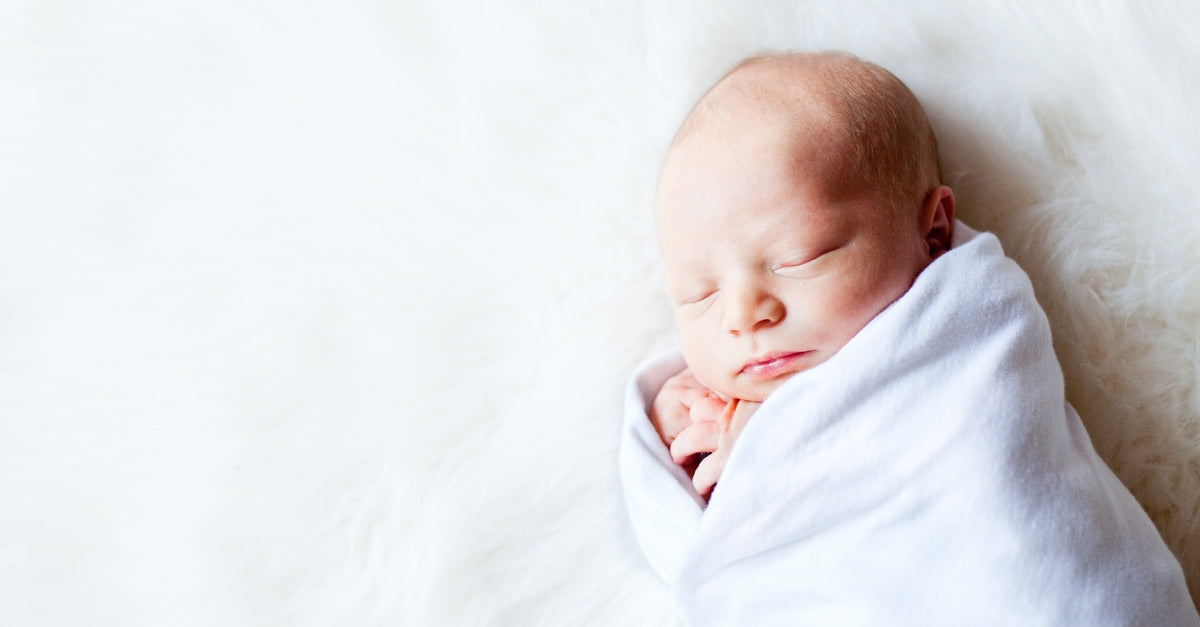 Newborn sleeping swaddled on white animal fur.
