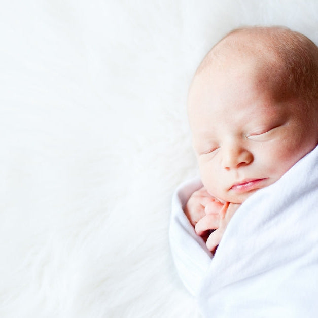 Newborn sleeping swaddled on white animal fur.