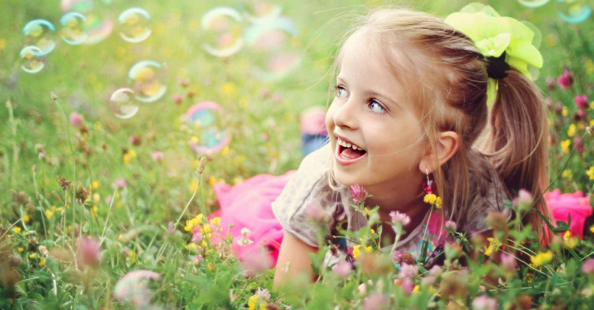 Girl laughing in a flower field with bubbles floating nearby.