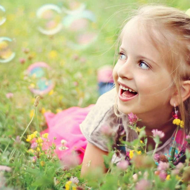 Girl laughing in a flower field with bubbles floating nearby.