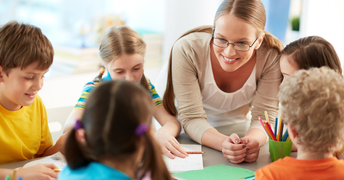 Teacher helping a group of children with a classroom activity at a table.