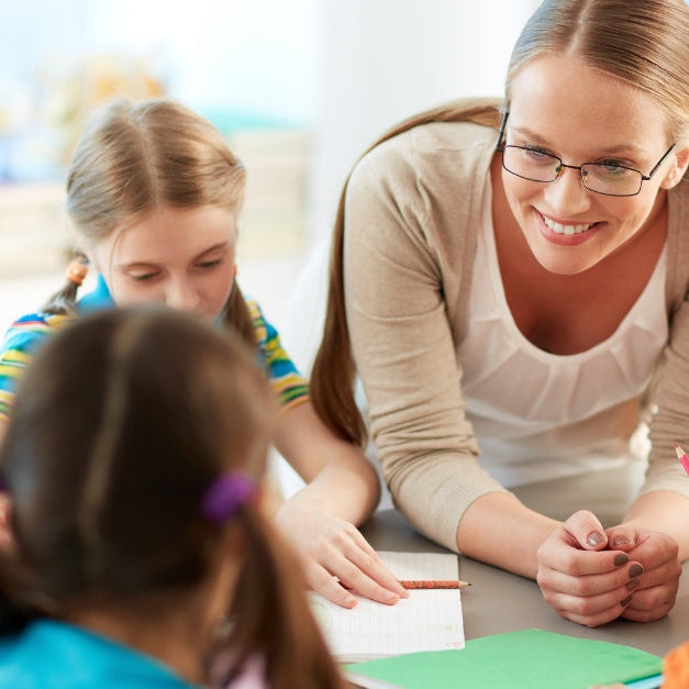 Teacher helping a group of children with a classroom activity at a table.