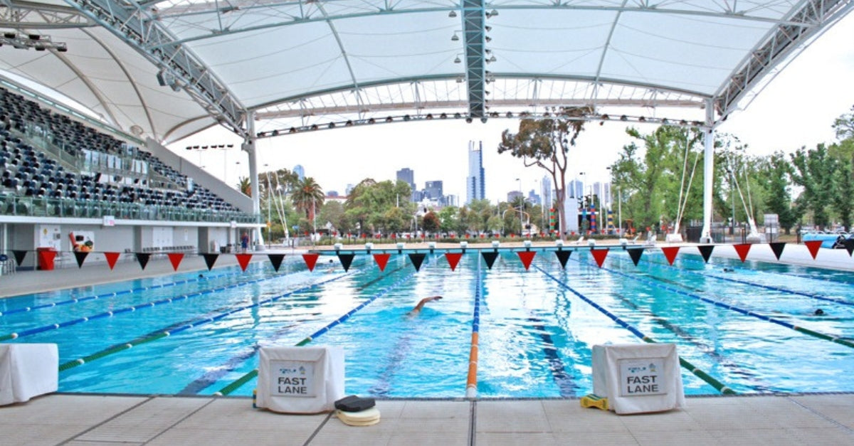 Outdoor lap pool with lane markers and city skyline in the background.