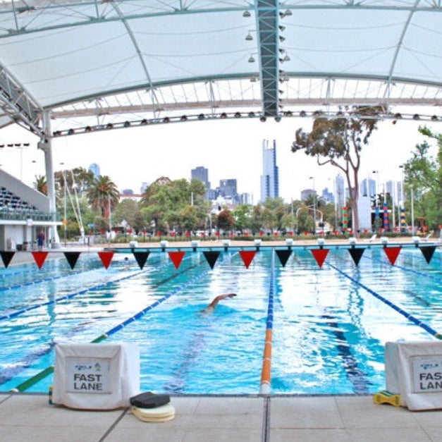 Outdoor lap pool with lane markers and city skyline in the background.