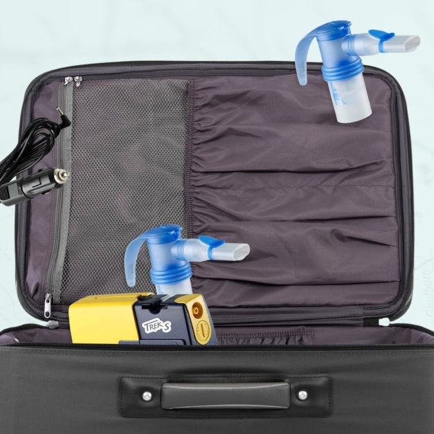 The PARI Trek S Portable Nebulizer System packed inside an open suitcase, with charger cable and second nebulizer attachment shown alongside.